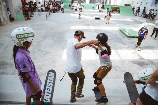 Photo of a skateboard class at Skateistan Cambodia with a coach holding hands with a student.